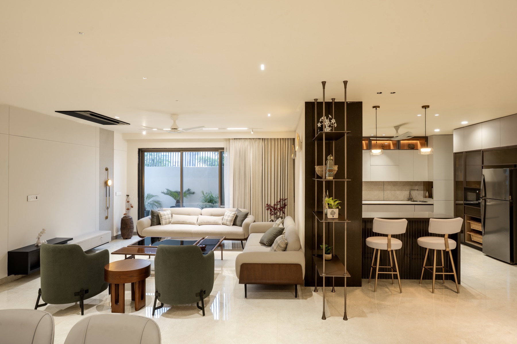 Open-plan living and island kitchen at Jain's House with sage armchairs, walnut joinery and brass details
